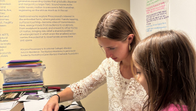Two people are creating an art project together in a gallery space. One is older and one is younger. 