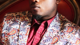Portrait of Jonah Mixon-Webster, he is wearing a floral print suit and a pink shirt, looking into the distance. 