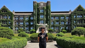 Hunter Leong stands in front of a university building in Korea whose walls are covered by moss