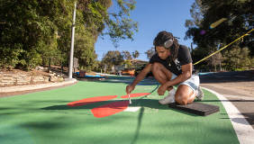 An Occidental College student paints a mural on a road on upper campus