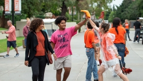 An O-Team member hi-fives a new first-year student walking on the sidewalk with his mother