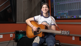 an occidental student posing for photo with guitar inside of music studio