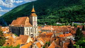 A quaint Romanian village with orange-colored roofs and a steeple in the middle against a lush green hillside