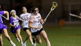 Occidental College women's lacross players running across a green field at a night game
