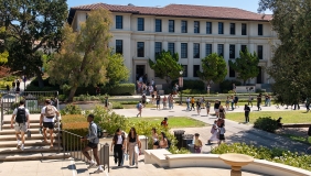 A view of Occidental College students on campus, entering Johnson Student Center and walking up steps with Fowler Hall in the background.