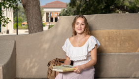 an occidental student sits on a bench with a book smiling on the los angeles campus.