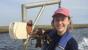 Zoe Kitchel stands on a boat holding a lobster specimen