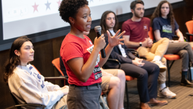 Previous campaign semester students sitting down, one standing holding a microphone.