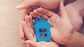 many hands hold a blue house-shaped cutout.