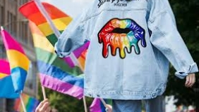Parade location featuring LGBTQ flats, a person with a denim jacket with a patch on it walks away from the camera.