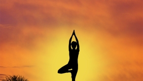 Silhouette of a person doing a yoga pose in front of a yellow sunset.