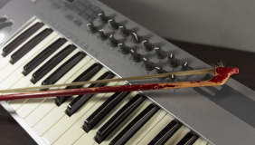 an electronic keyboard controller with a violin bow resting on its keys