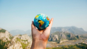 The foreground shows a hand holding a small globe, with mountains in the background