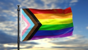 A brightly colored PRIDE rainbow and trans flag against a sunny sky