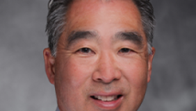 A headshot of doctor Linton Yee who wears a blue business shirt with a gray backdrop.