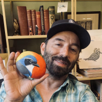 Man holding rock with bird art in front of bookshelf