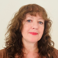 Mo has curly medium brown hair and is wearing a brown jacket and black top