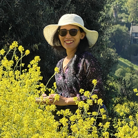 Tuyetdong Phan-Yamada headshot in a field of flowers wearing a hat