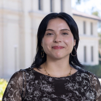 Kim is wearing a black dress with white print and is standing in front of a building