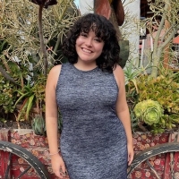 Mia Villegas, a young woman in a gray dress, smiles in front of a cart of desert plants.