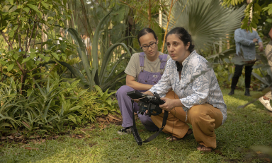 Anahid Yahjian, right, a female Armenian director crouching down with a coworker in a green outdoor setting