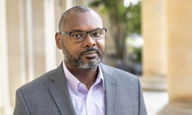 Professor Derrick Spires headshot with glasses and grey coat