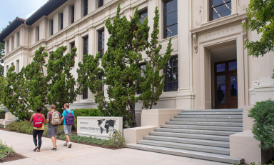 A view of the front of Johnson Hall with three students passing on the sidewalk