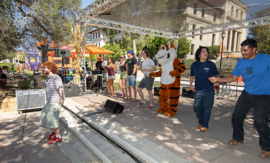 Occidental College students dancing in a group on campus with Oswald the Tiger