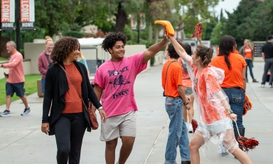 An O-Team member hi-fives a new first-year student walking on the sidewalk with his mother