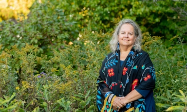 Robin Wall Kimmerer photographed outdoors in front of a green setting with wildflowers