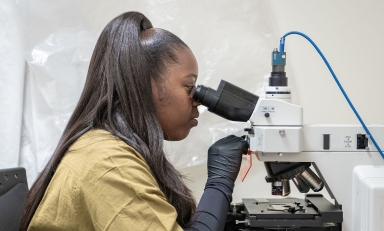 Daisy Ademoye looking into a powerful microscope in the Mind and Brain lab