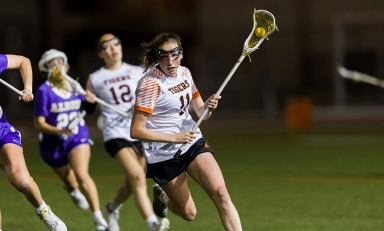 Occidental College women's lacross players running across a green field at a night game