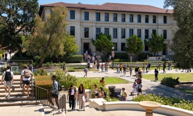 A view of Occidental College students on campus, entering Johnson Student Center and walking up steps with Fowler Hall in the background.