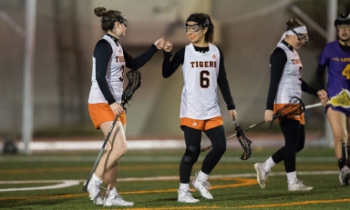 Two Oxy students playing women's lacrosse fist-bump each other