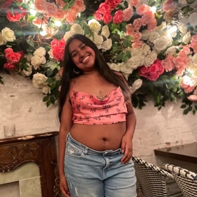 Yareimy is standing in front of a wall hanging made of roses 