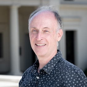 David is wearing a black shirt with white print and is standing in front of a building