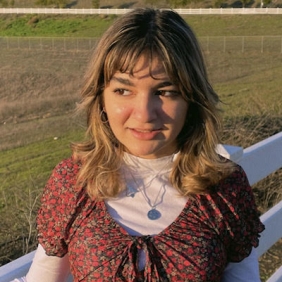 A young person looks off to the side and is lit by golden hour light. 