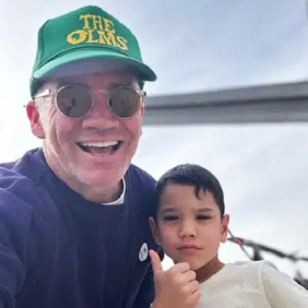 Ian Montone in a green baseball hat and a young child giving the thumbs up