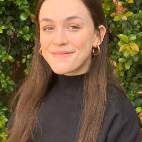 Sela is wearing a black shirt with greenery in the background