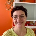 Laura is smiling and standing in front of an orange-red wall