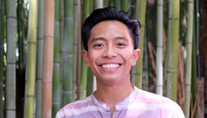 a young man smiles in front of bamboo stalks
