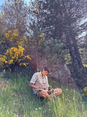 An Occidental College student sits in the grass in an outdoor setting, taking field notes