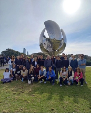 A group of students posing on a lawn next to a silver abstract sculpture