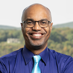 Ron Buckmire headshot in purple shirt and blue tie