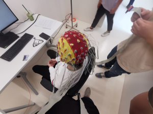 Person wearing cap covered in wires sitting in front of a computer