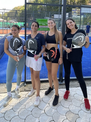 Four young women holding pickleball rackets next to a court